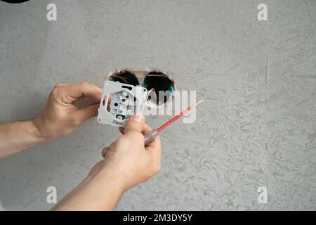electrician connects the sockets to the electrical wires on the wall using a screw driver, close up Stock Photo