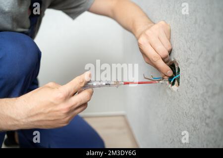 electrician connects to the electrical wires on the wall using Screwdriver, close up Stock Photo