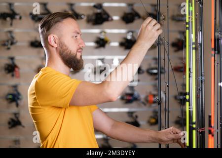 man shopper choosing fishing rod in the fishing store, side view Stock Photo
