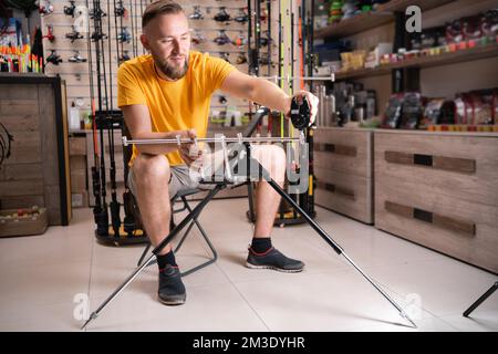 Man choosing fishing rod stand in sports shop. Copy space Stock