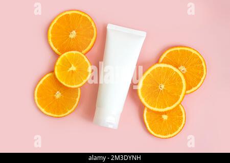 Flacon for cream and orange slices on light pink background. Container for body lotion, toiletry. Tube for professional care products. Skincare and ad Stock Photo