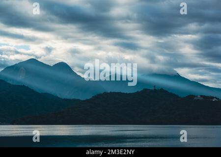 Mountains surrounded by clouds. Crepuscular Ray shines on the village. Chaowu Pier, Sun Moon Lake National Scenic Area. Nantou County, Taiwan Stock Photo