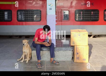 A young Indian man sitting next to a stray dog on a platform at Chhatrapati Shivaji Maharaj Terminus in Mumbai, India Stock Photo