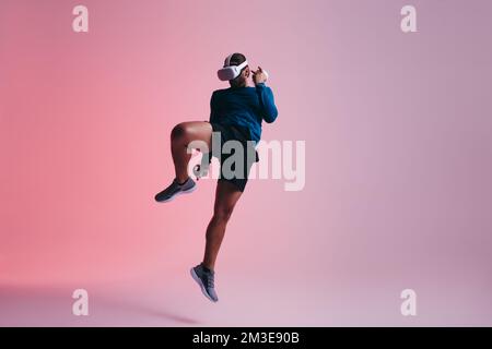 Kickboxing in virtual reality. Active young man jumping mid air while wearing a virtual reality headset. sporty young man exploring immersive virtual Stock Photo