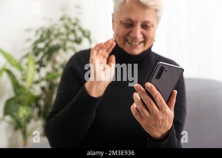 Happy mature old 60s woman holding smartphone using mobile phone app for video call, laughing while watching funny video, feeling excited winning Stock Photo