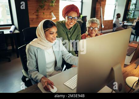 Three cheerful businesswomen having a discussion while looking at a computer screen in an office. Multicultural businesswomen working as a team in a m Stock Photo