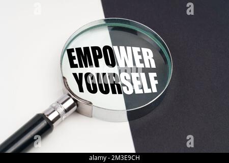 Business concept. On the surface, which is half black and white, lies a magnifying glass inside which is written - EMPOWER YOURSELF Stock Photo