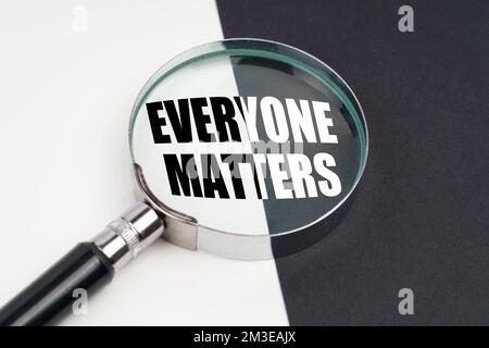 Business concept. On the surface, which is half black and white, lies a magnifying glass inside which is written - EVERYONE MATTERS Stock Photo