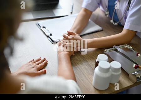 A female doctor holding her patient's hands on the table while discussing the treatment plan. cropped and close-up image Stock Photo