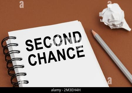 Business and finance concept. On a brown surface lies a pen, crumpled paper and a notepad with the inscription - SECOND CHANCE Stock Photo