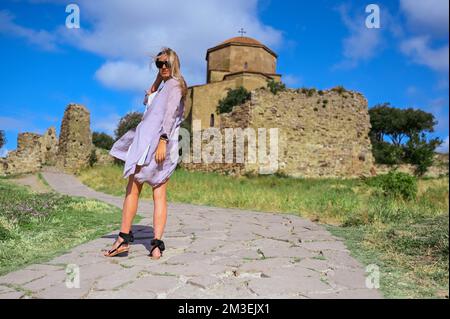 Happy young traveling woman blonde tourist outdoors in ancient Europe fortress ruins. Beautiful female on summer holiday vacation, active lifestyle concept. Jvari Monastery, Mtskheta, Georgia Stock Photo