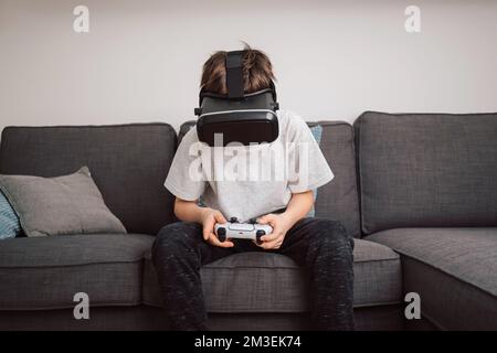 Caucasian boy enjoying at home, gaming using VR box, virtual reality goggles, and simulator, moving and physically interacting with a virtual world Stock Photo