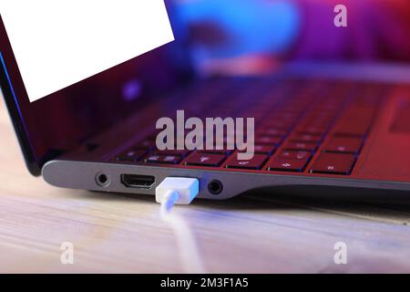 old laptop with usb cable on table and pink background Stock Photo