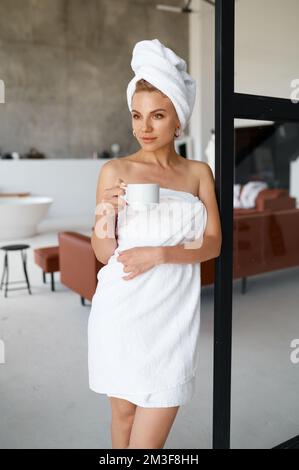 Portrait of young woman wrapped in towel drinking hot tea or coffee Stock Photo