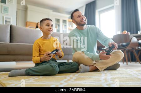 Happy father and son playing video game sitting on floor Stock Photo