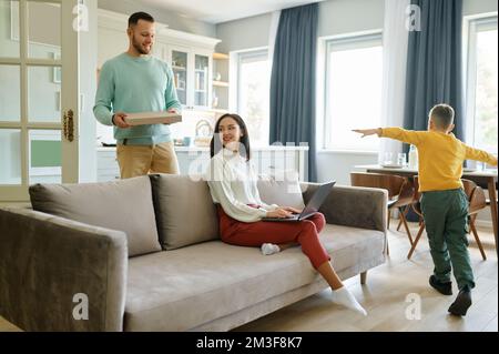 Wife working on laptop while husband orders pizza for lunch Stock Photo