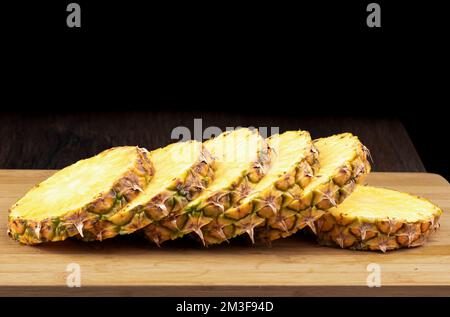Sliced ripe pineapple on a wooden cutting board against a black background. Copy space. Stock Photo