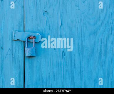 Outdoor wooden panel locked shut with a padlock. The panel, latch, and lock are painted blue. A small amount of white bird dropping is on the latch. Stock Photo