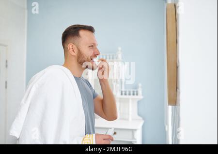 Man brushing teeth in bathroom looking at mirror side view shot Stock Photo