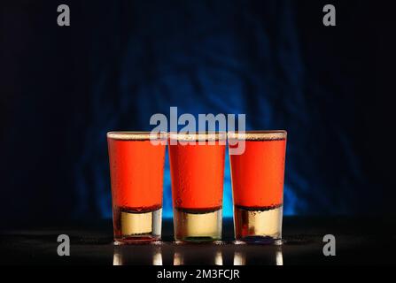 three glasses with red alcohol on a black background with a blue gradient Stock Photo