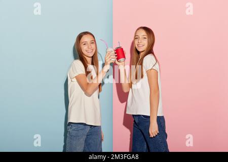School age girls, sisters friends wearing white t-shirts and jeans communicate isolated over pink-blue background. Concept of love, friendship, family Stock Photo
