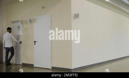 Young man walking inside the public bathroom inside shopping mall. HDR. Man entering toilet room Stock Photo