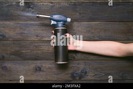 a portable gas soldering iron is burning in the girl's hand. gas cylinder 220 grams in a woman's hand. Stock Photo