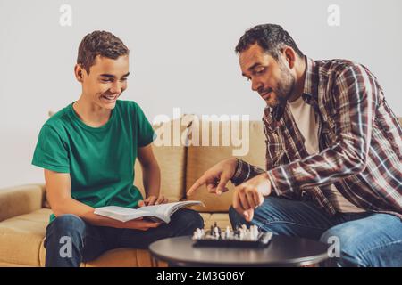 Father and son are playing chess at home. Boy is learning about chess. Stock Photo