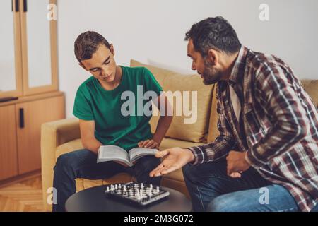 Father and son are playing chess at home. Boy is learning about chess. Stock Photo