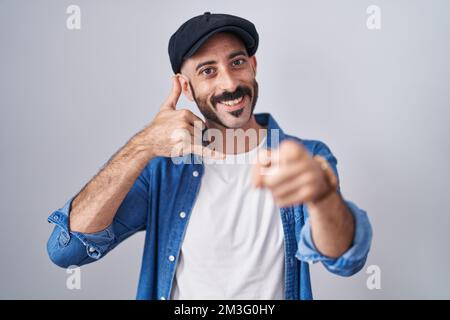 Hispanic man with beard standing over isolated background smiling doing talking on the telephone gesture and pointing to you. call me. Stock Photo