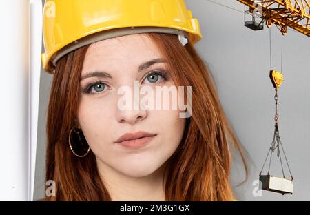 Young female redhead worker of construction site wearing a safety vest and hardhat - Construction site background with focus on eyes Stock Photo