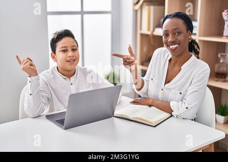 Young mother and son doing homework with laptop smiling happy pointing with hand and finger to the side Stock Photo