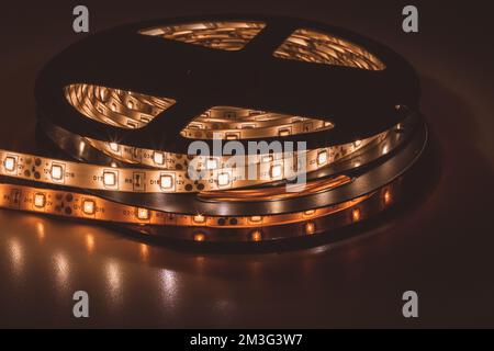 From above bobbin with roll of glowing LED strip lighting placed on table in dim room Stock Photo