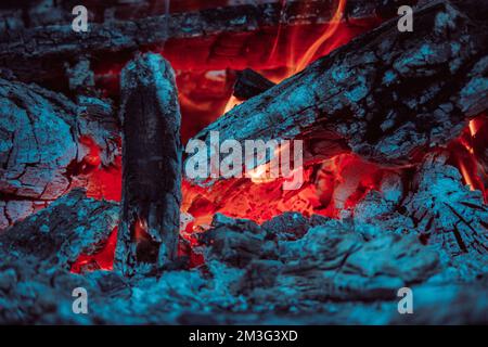 Charcoal and logs covered with ash burning with bright red fire in campfire at night Stock Photo