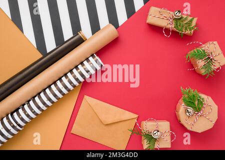 Christmas gift or present box wrapped in kraft paper with decoration on red background from above. Flat lay style. Stock Photo