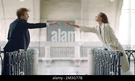 Couple reaches out to each other. Action. Romantic couple reach out with their hands at distance. Elegant couple are stretching on different sides of Stock Photo