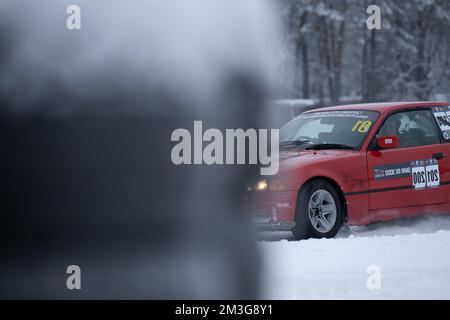 12-12-2022 Riga, Latvia  a red car is parked in the snow with a yellow and black sign on it's windshield and a person is looking at it. . Stock Photo