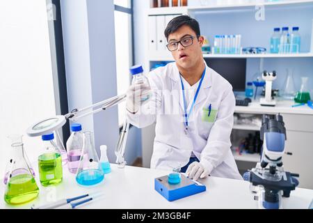 Down syndrome man wearing scientist uniform measuring liquid at laboratory Stock Photo