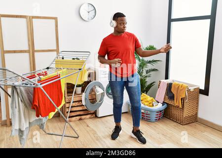 Young african man wearing headphones dancing at laundry room Stock Photo