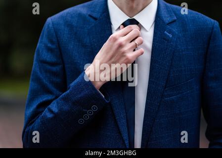 Elegant man tying his tie over black shirt. Adjusting tie. Black and violet. Young business man dressing, isolated on black background. Groom adjustin Stock Photo