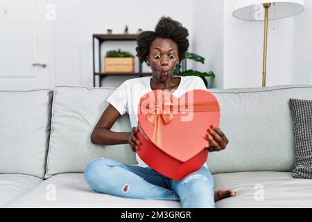African young woman opening romantic gift making fish face with mouth and squinting eyes, crazy and comical. Stock Photo