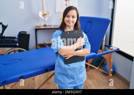 Down syndrome woman wearing physiotherapy uniform holding clipboard at physiotherapist clinic Stock Photo