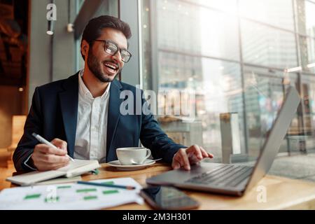 Indian businessman is making notes in notepad during working day in cafe. Blurred background Stock Photo