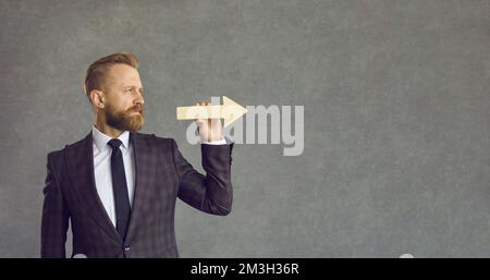 Serious businessman holding arrow and looking straight ahead on grey copy space background Stock Photo