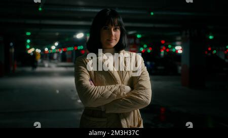 Parking lot dark background alone confident girl lady female worker manager employer entrepreneur woman standing with crossed hands pose crossing arms Stock Photo