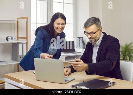 Smiling office colleagues using laptop together, discussing project Stock Photo