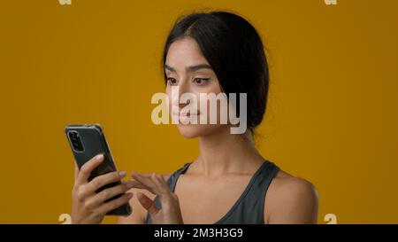 Close up Indian ethnic woman girl lady female smile browsing cell smartphone looking at camera with recommendation gesture swipe in mobile phone Stock Photo
