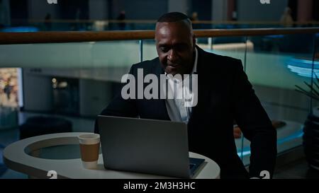 Middle-aged adult ethnic entrepreneur man with laptop working in shopping mall company talk video call conference typing online. African businessman Stock Photo
