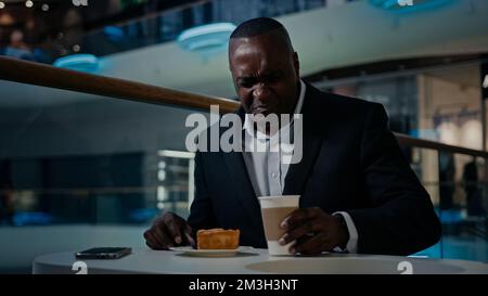 African American middle-aged businessman entrepreneur cafe visitor man sitting eating in cafeteria dissatisfied with bad cake disgust pie dessert Stock Photo