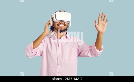 Joyful young man enjoying using virtual reality glasses on pastel light blue background. Stock Photo